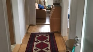Un couloir avec un tapis à motifs, un plancher en bois, un canapé, un meuble et une porte.