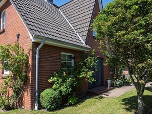 A brick house with a tiled roof, a front door, and a small front yard with a tree and shrubs. - Amselhaus - Beautiful 120 m² single-family home with 5 rooms and a large yard, suitable for up to (Sylt)