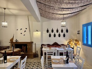 Un comedor con mesas dispuestas para comer, una chimenea y utensilios de cocina colgados en la pared.
