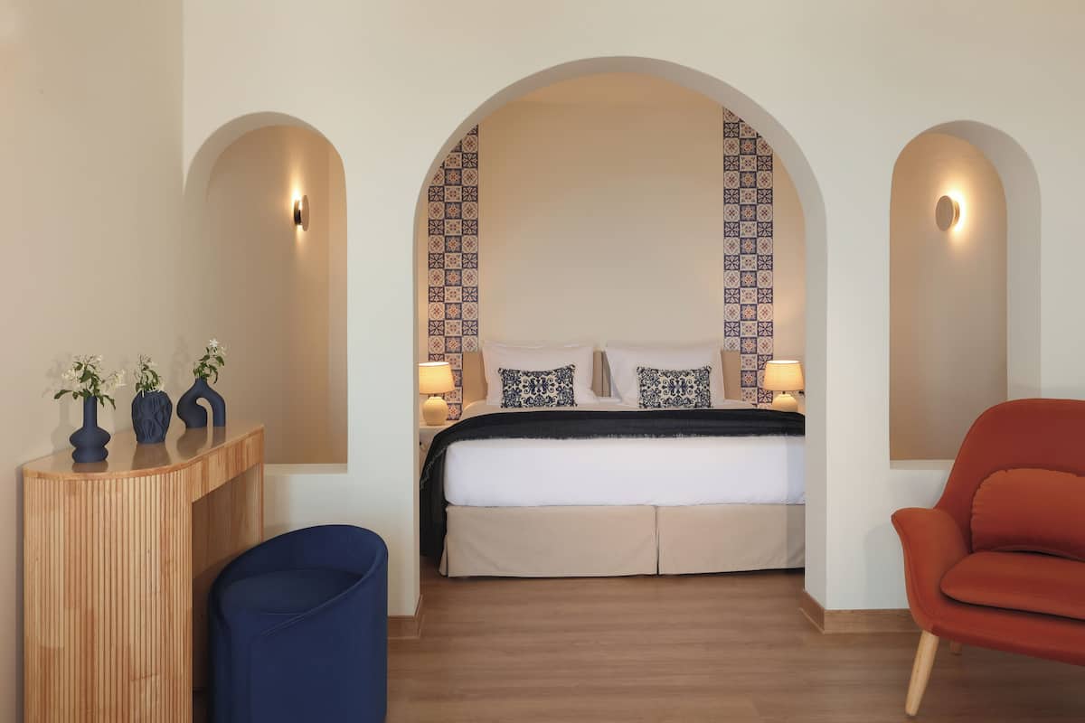 Een slaapkamer met een bed, een houten nachtkastje, een blauwe stoel en een rode stoel.
