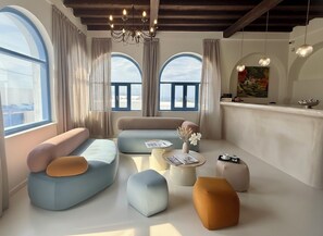 A modern living room with a sofa, ottomans, a coffee table, and a dining area with a bar. - White Pearl Laokasti Suites (Oia)