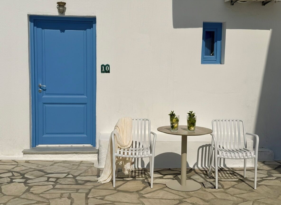 A blue door, a small window, and two white chairs with a table between them.