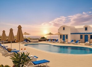 A pool area with lounge chairs, umbrellas, and a building with a blue door. - White Pearl Laokasti Suites (Oia)