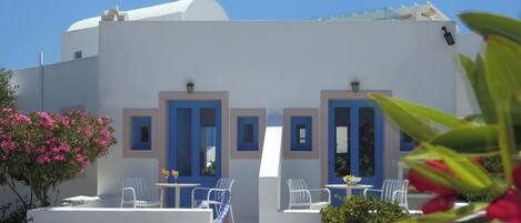 A white building with blue doors and windows, outdoor seating with white chairs, and a potted plant.