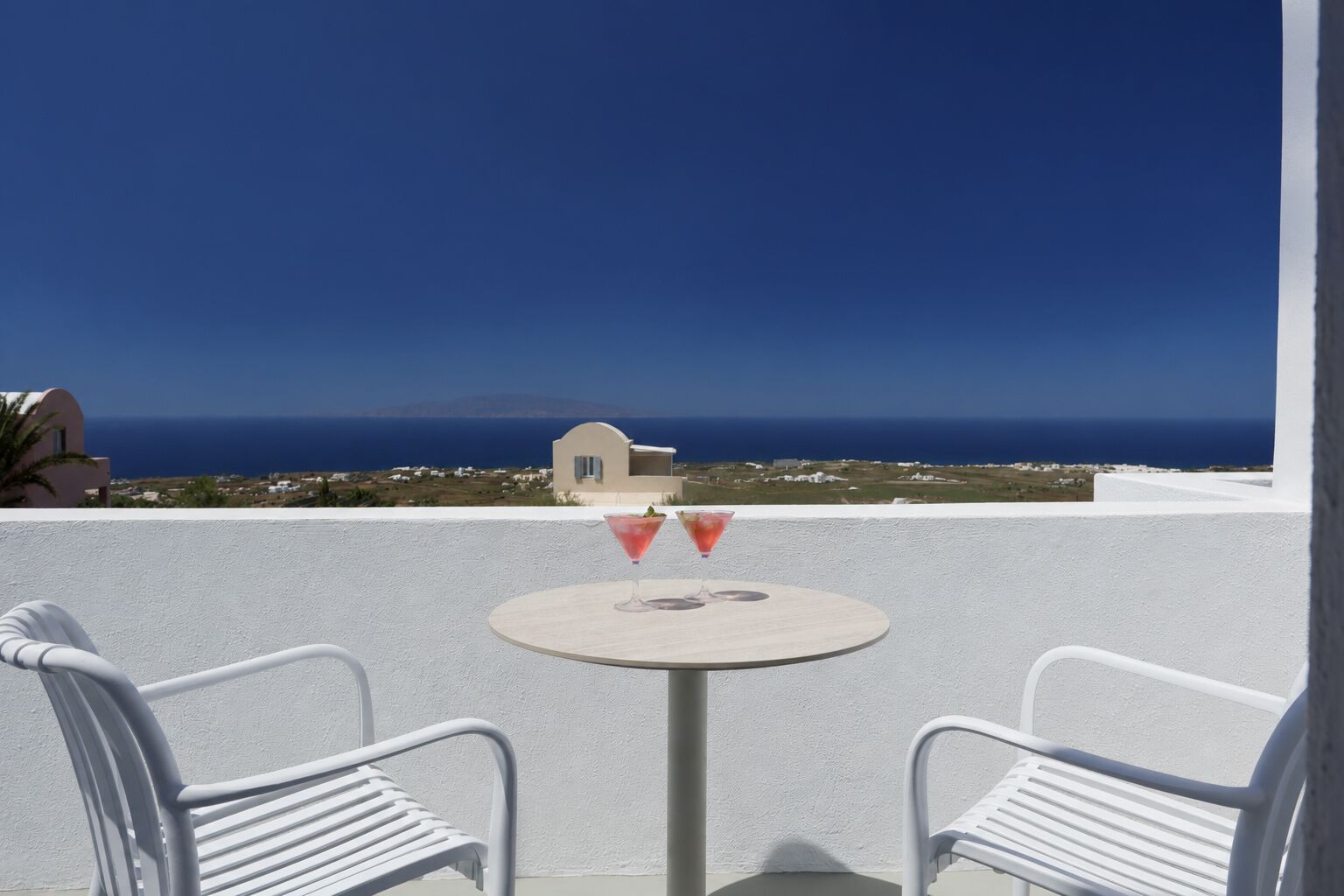 A white chair and table on a balcony with a view of the sea and distant buildings.