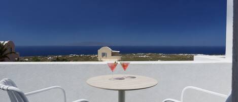 A white chair and table on a balcony with a view of the sea and distant buildings.