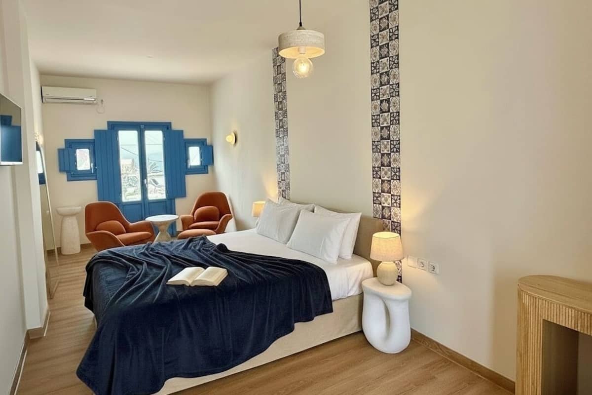 Une chambre Ă coucher comprenant un lit, deux chaises, une table de chevet, une lampe et un luminaire suspendu.