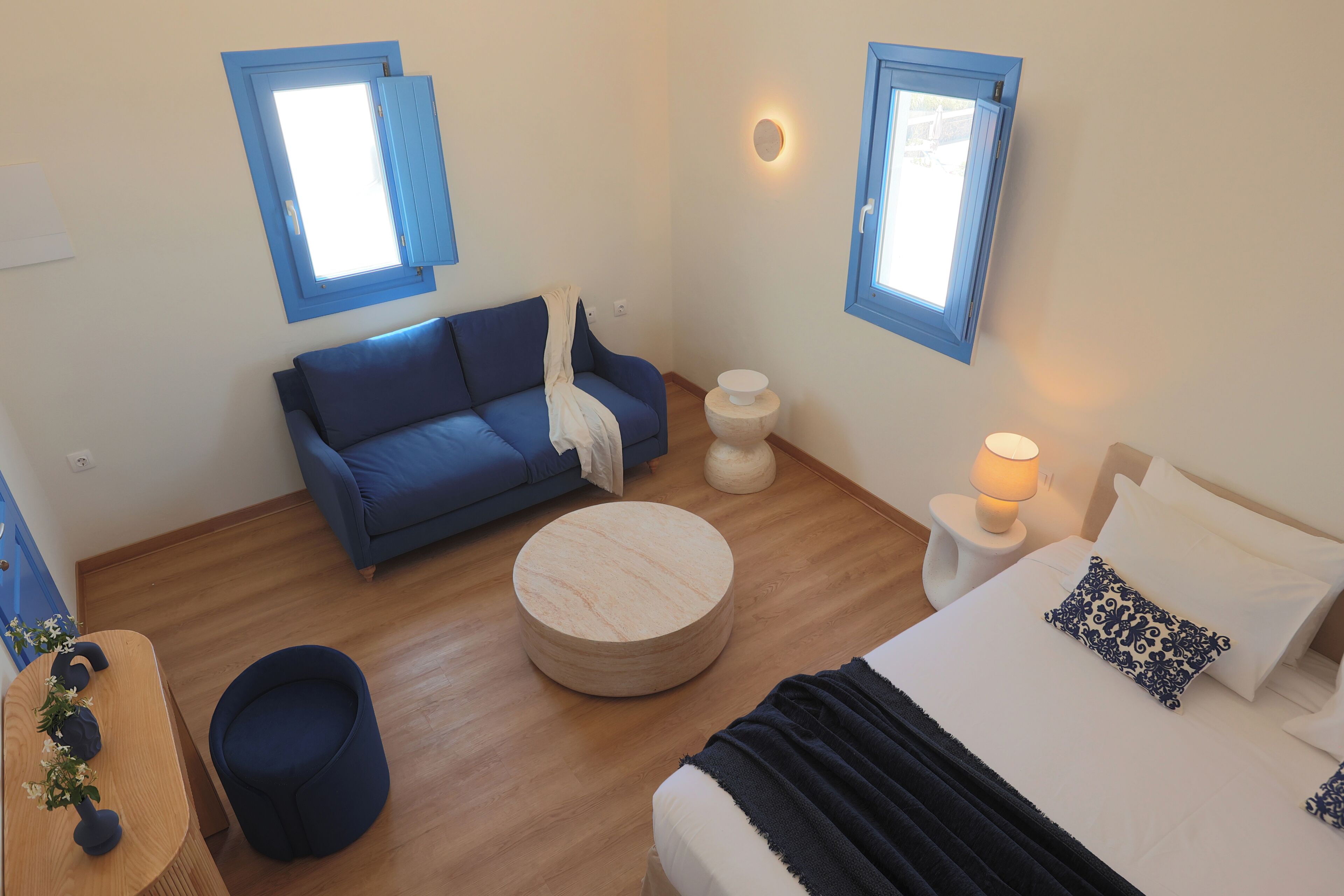 A room with a bed, a blue sofa, a round wooden table, and two small side tables.