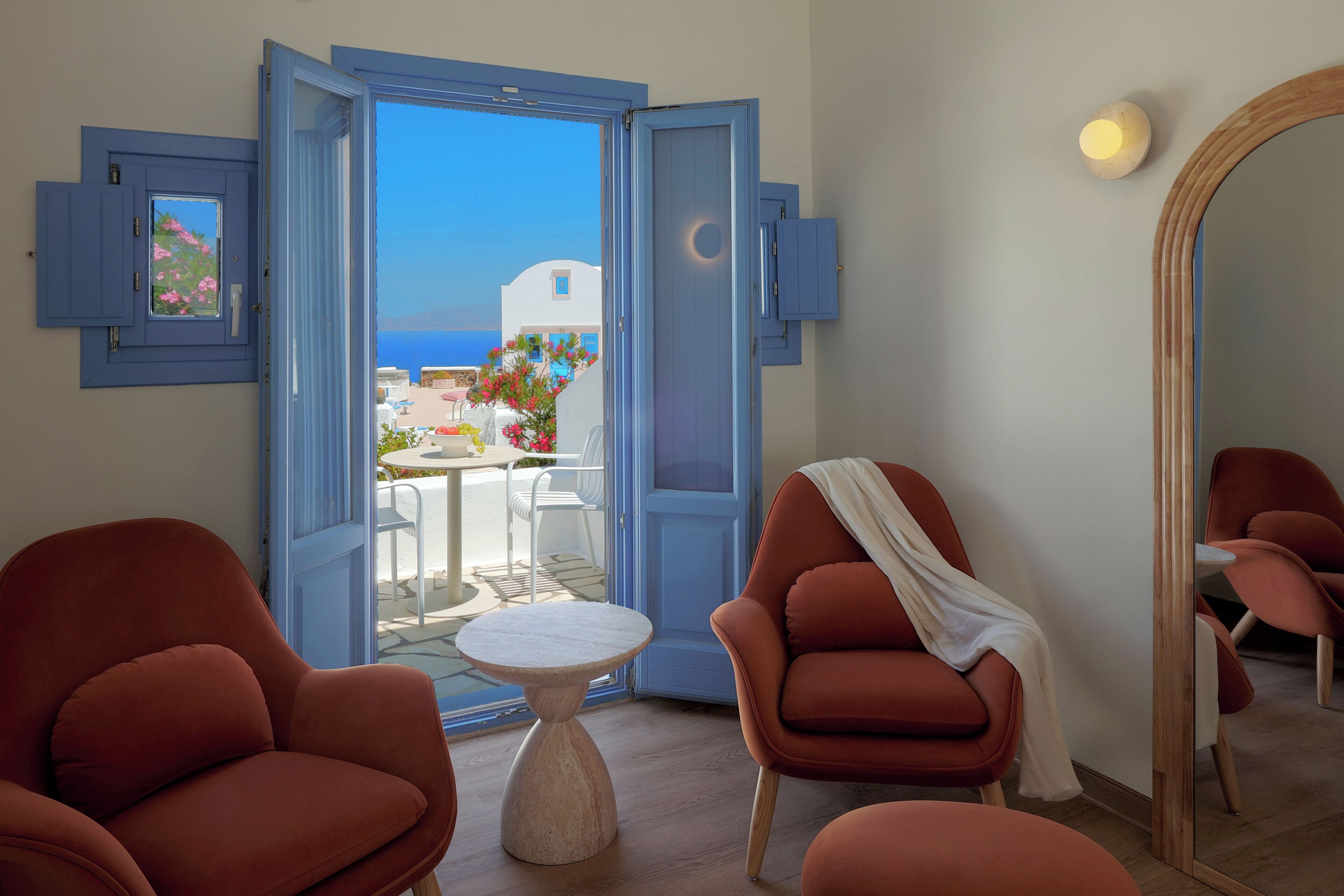 A room with a view of the sea, a balcony with outdoor furniture, and a mirror.
