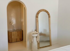 Un baño con tocador de madera, un espejo con marco de madera y una toalla sobre un lavabo blanco pedestal.