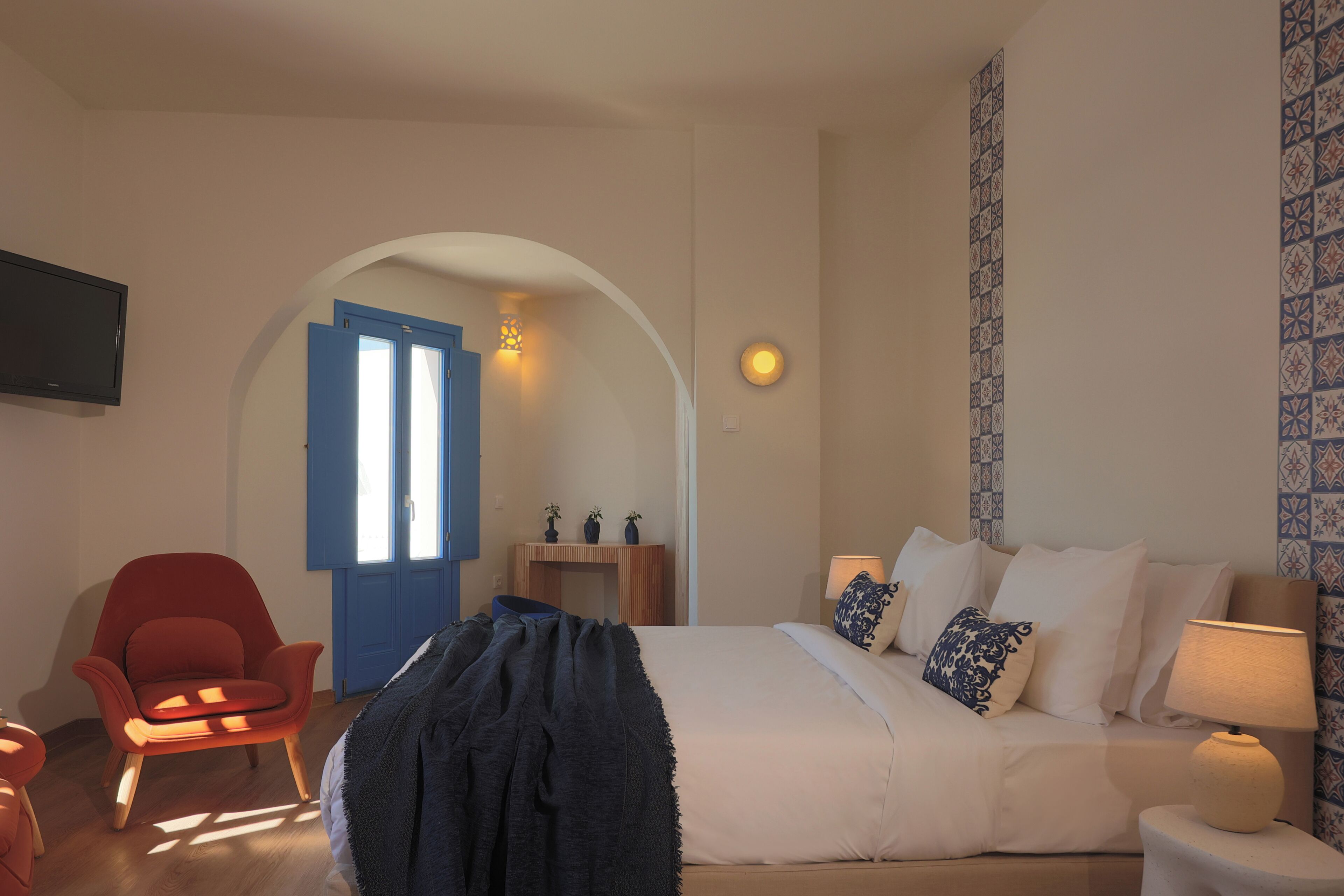 A bedroom with a bed, bedside lamp, and a TV mounted on the wall.