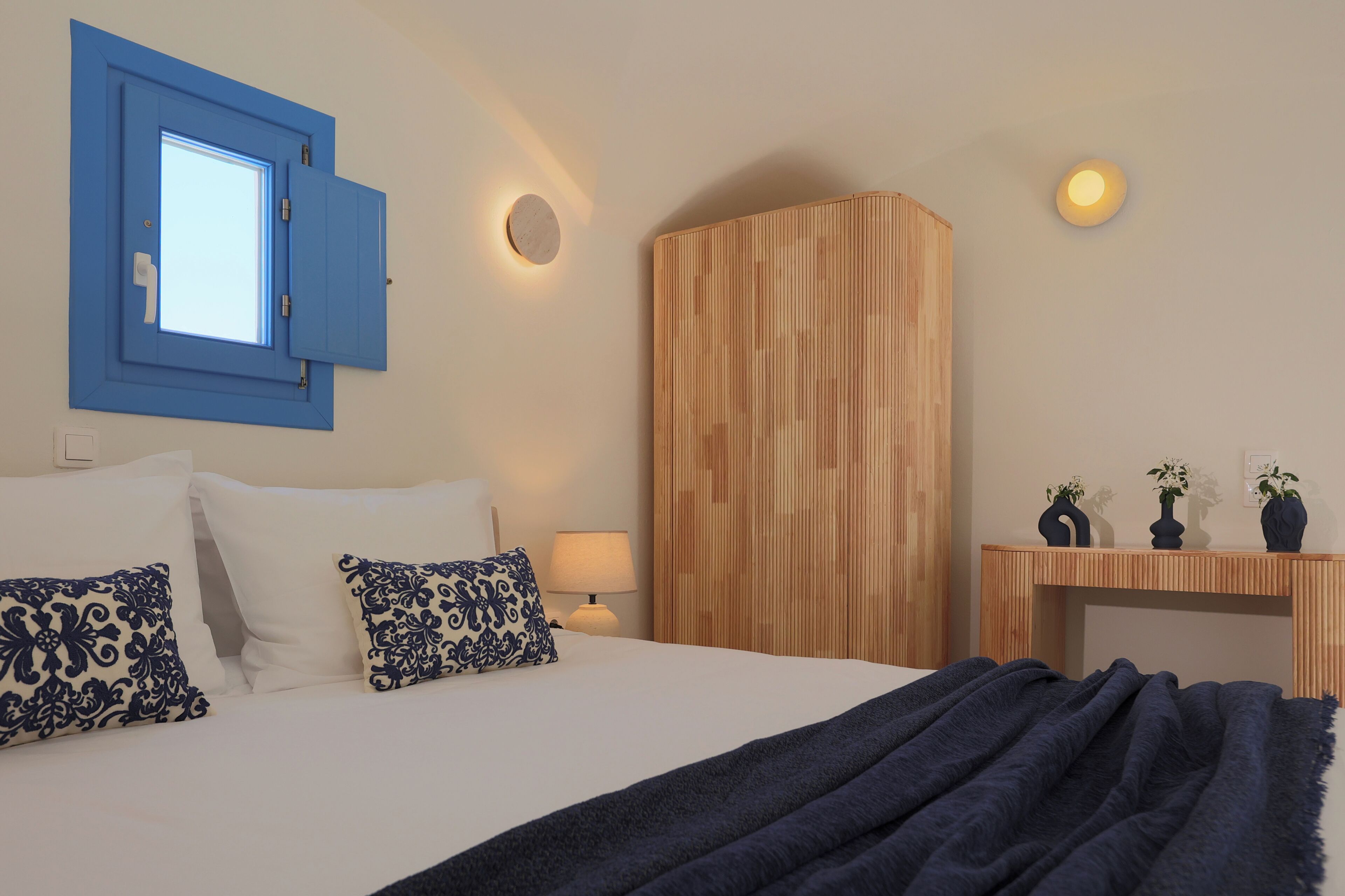 Una camera da letto con un letto, cuscini, un comodino, una lampada, un armadio in legno e una finestra con persiane.