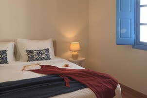 Una cama con un plaid rojo, un perchero de madera y una lámpara sobre una mesita de noche.