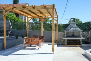 Eine Terrasse im Freien mit einer Holz-Pergola, einem Grill und Sitzgelegenheiten.