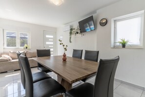 Ett modernt matområde med ett träbord och svarta stolar, en platt-TV som är monterad på väggen och ett fönster med en växt i.