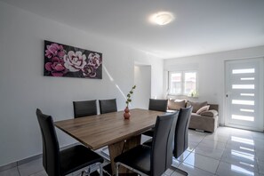 A dining area with a wooden table and chairs, a painting of flowers on the wall, and a view of the living room through an open door. - Villa Mia near Zadar (Glavica)