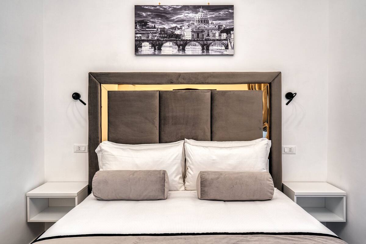 Un dormitorio con una cama grande, un cabecero con detalles dorados, dos mesitas de noche y un cuadro colgado en la pared.