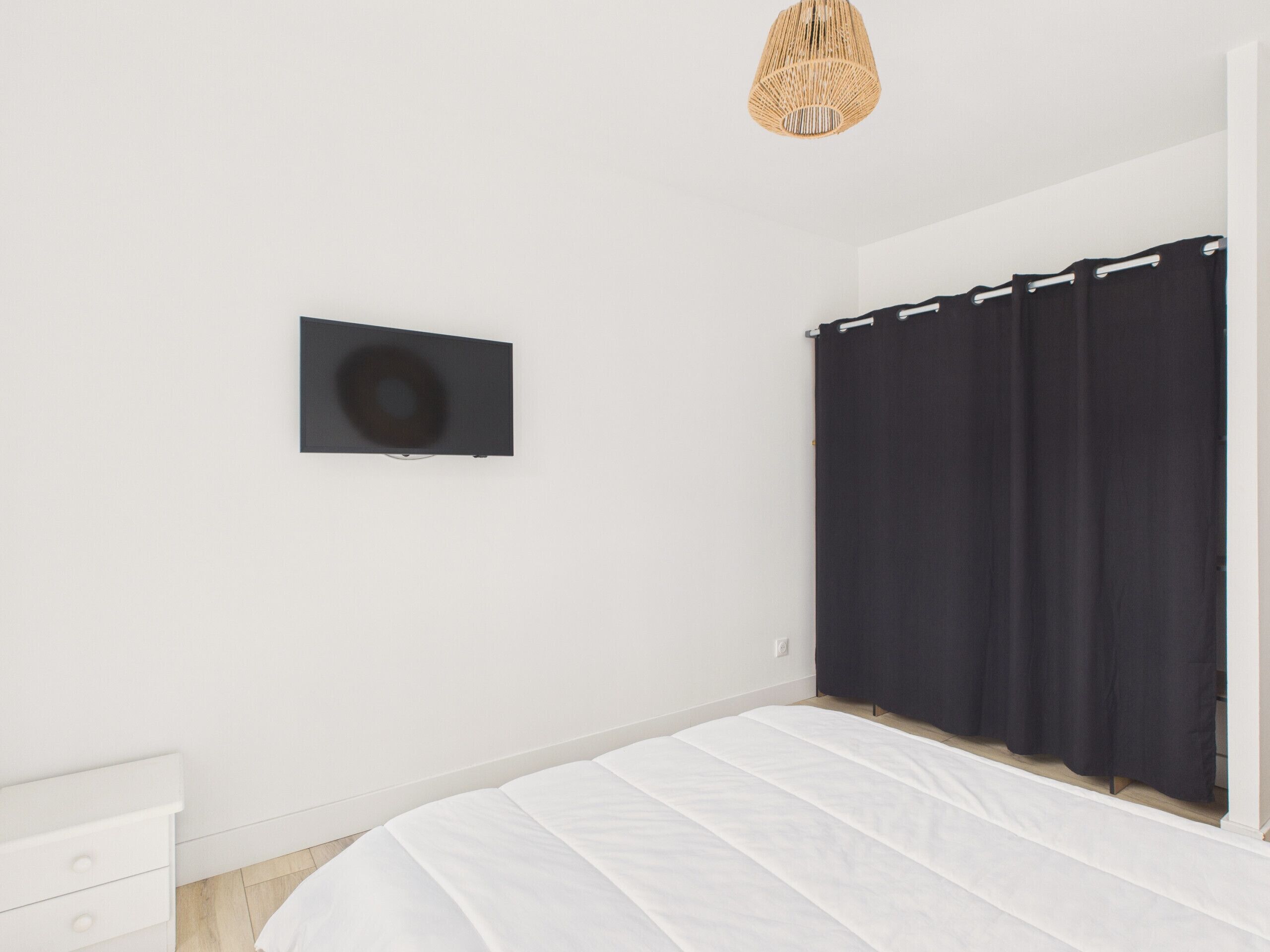 Un dormitorio con cama, televisor montado en la pared y ventana con cortinas.