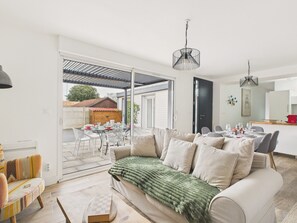 A modern living room with a sofa, a dining table set for four, and a kitchen area visible through an open door. - Comfort for 6 to 800 m from the beach (La Plaine-sur-Mer)
