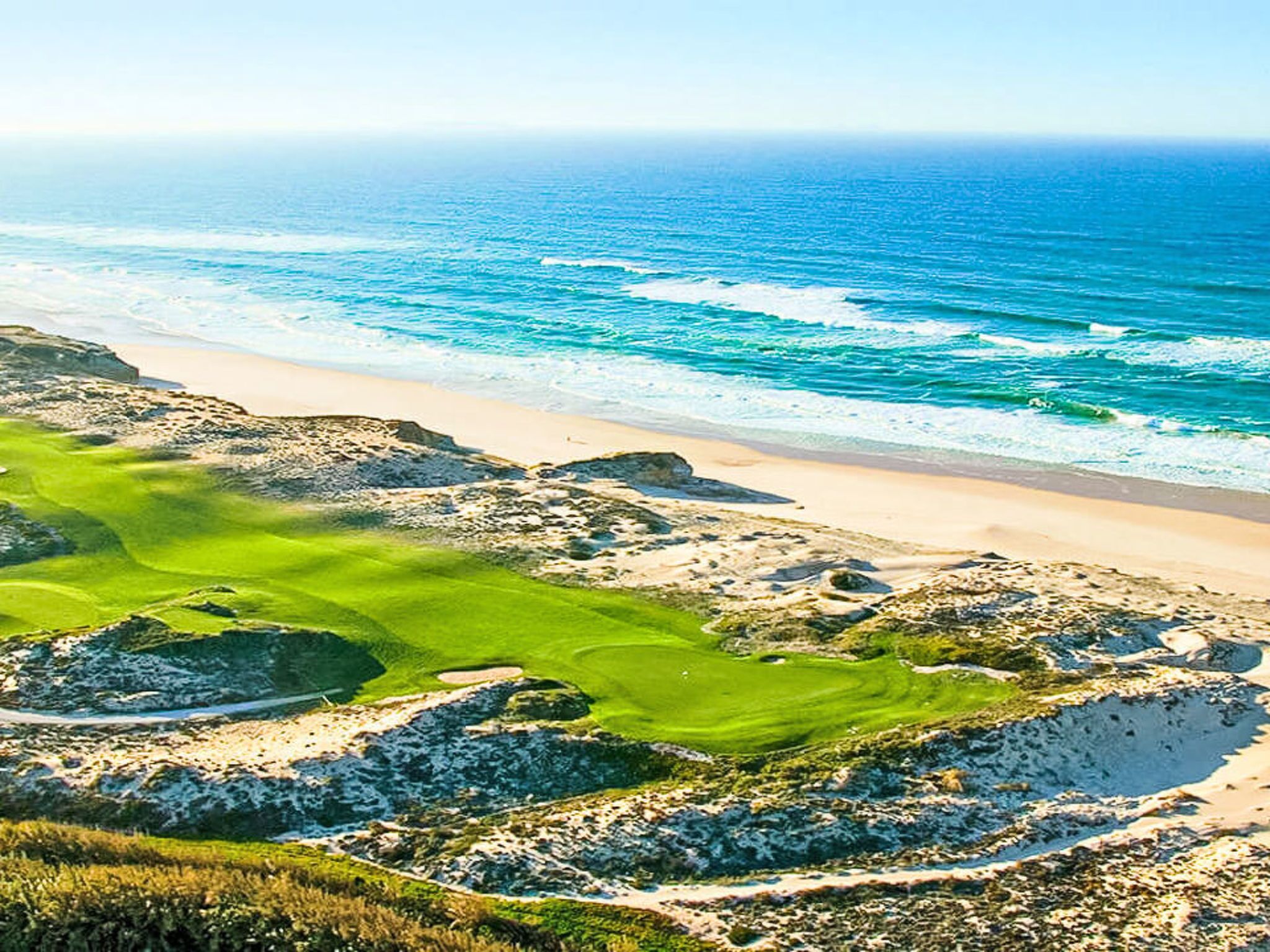 Eine Küstenlandschaft mit Strand, felsigem Gel ände und einem Golfplatz.