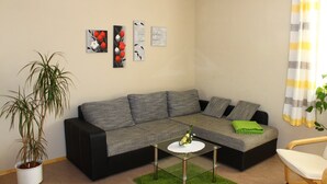 Ein Wohnzimmer mit einer Eckcouch, einem kleinen Tisch, einer Topfpflanze und Wandbildern.