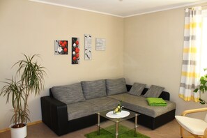 A living room with a sectional sofa, a small table, a potted plant, and wall art. - XXL Ferienhaus in Struppen (Struppen)