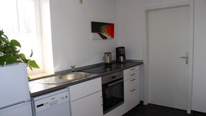 Une cuisine moderne avec des meubles blancs, un lave-vaisselle encastré, une machine à café et un four à micro-ondes.