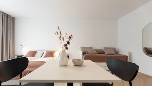 Ein modernes Wohnzimmer mit einem weißen Sofa, einem Couchtisch mit Dekoration und einem Essbereich mit Tisch und schwarzen Stühlen.