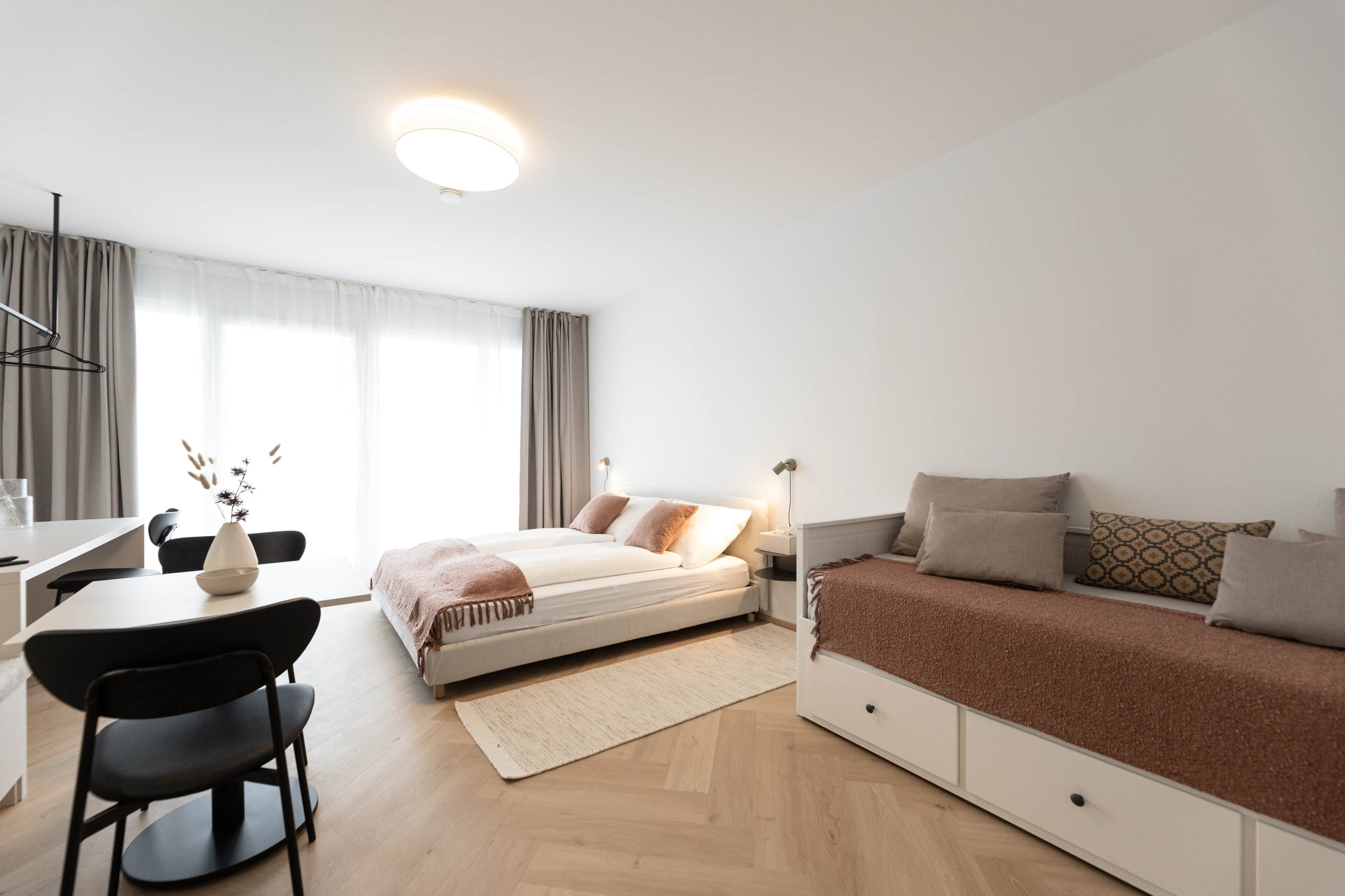 A modern bedroom with a bed, bedside table, and a desk with a chair.
