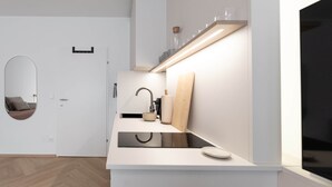 Eine moderne Küche mit weißer Arbeitsplatte, Spüle und Spiegel. Eine Tür mit Spiegel an der Wand und ein Holzregal über der Arbeitsfläche.