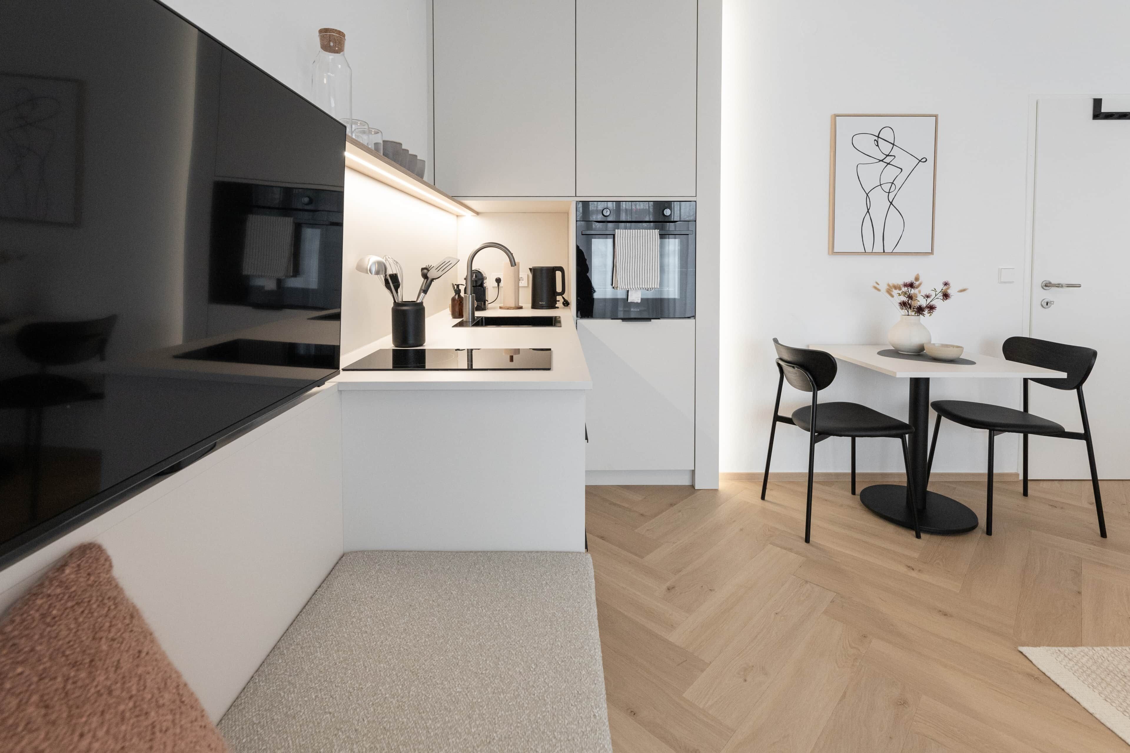 Een moderne keuken met een zwart aanrecht, roestvrijstalen apparatuur en een eethoek met twee stoelen en een tafel.