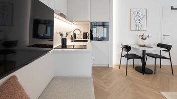 Een moderne keuken met een zwart aanrecht, roestvrijstalen apparatuur en een eethoek met twee stoelen en een tafel.