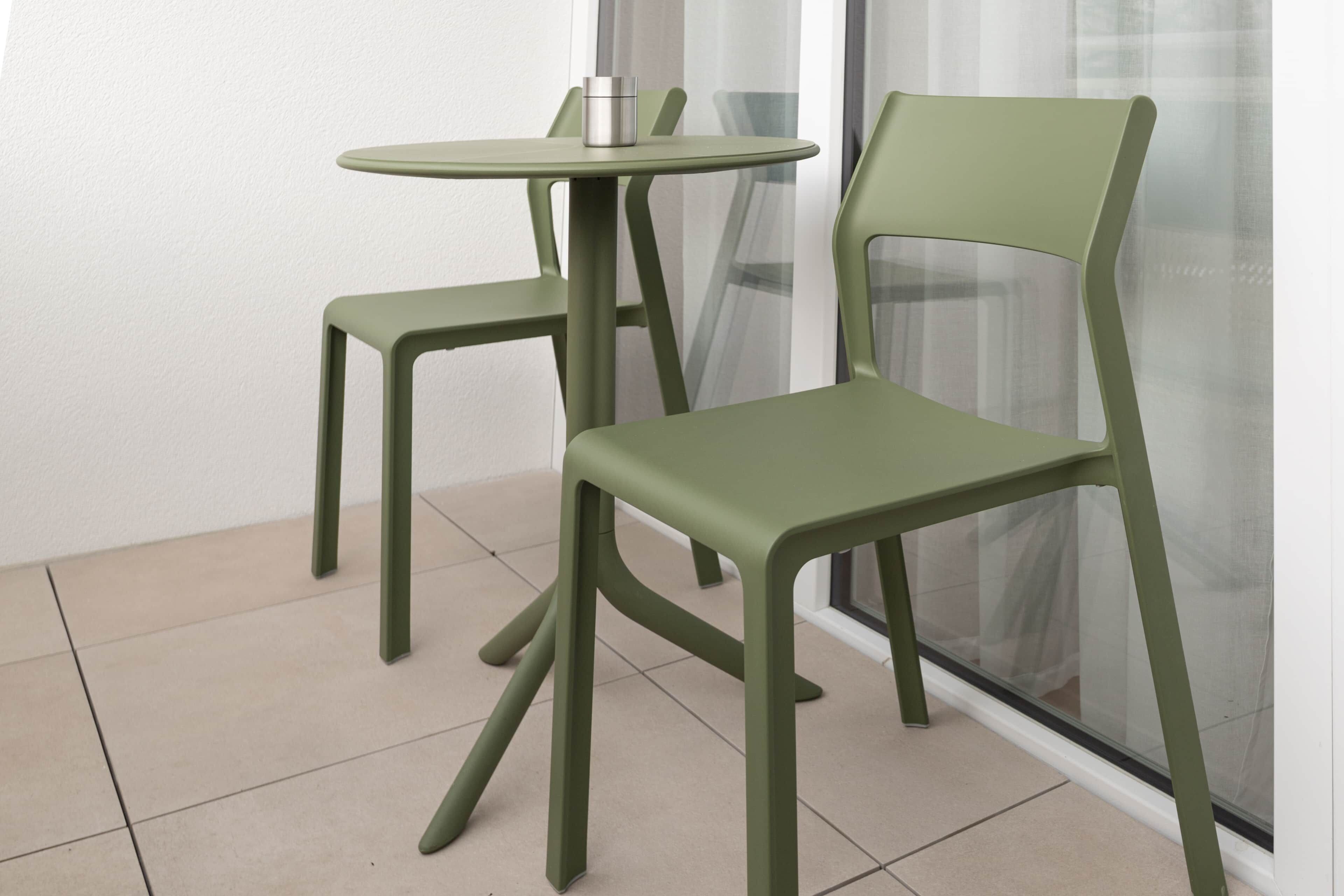 Un tavolino e una sedia moderni, di colore verde, posti in un angolo con vista su una finestra.