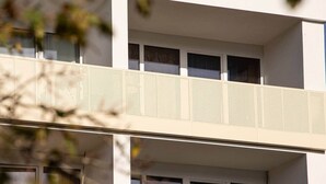 Ein modernes Gebäude mit flacher Fassade, zahlreichen Fenstern und einem Balkon mit Lochmuster.