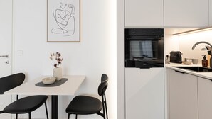 A modern kitchen with white cabinets, a black oven, and a dining area with a white table and black chairs.