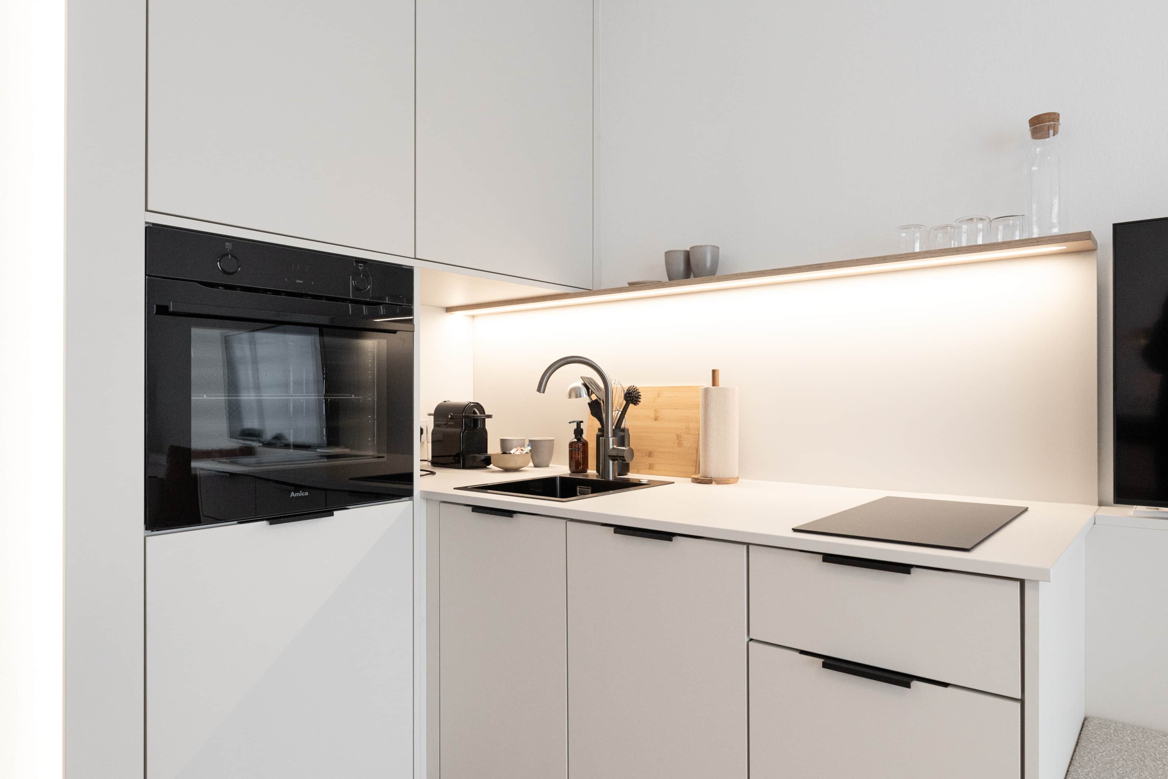 Eine moderne Küche mit weißen Schränken, einem Einbauofen, einem Spülbecken und einer Arbeitsplatte mit Kaffeemaschine und Tablet.