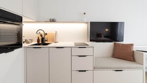 A modern kitchen with a built-in oven, a sink, and a flat-screen TV mounted above the counter.
