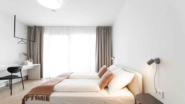 A modern bedroom with a bed, bedside table, and a desk with a chair.