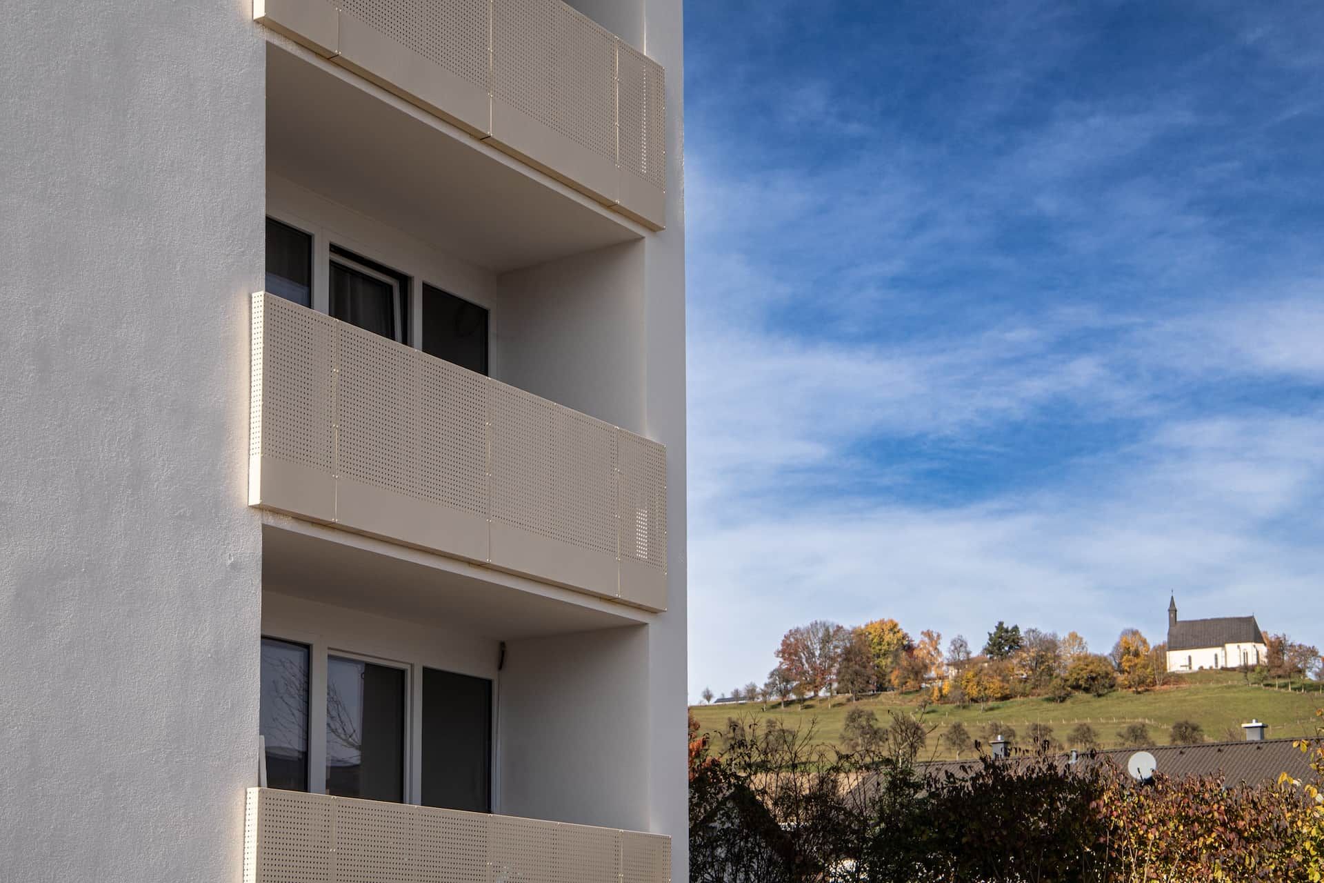 A building with a balcony, a window, and a view of a church on a hill.