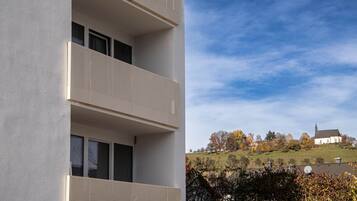 A building with a balcony, a window, and a view of a church on a hill.