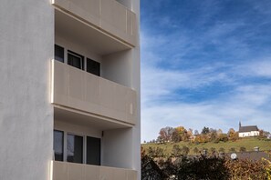 Un edifici amb un balcó, una finestra i vista d'església damunt d'un turó.