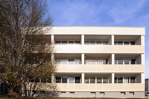 A multi-story building with a flat facade, large windows, and a tree in the foreground.