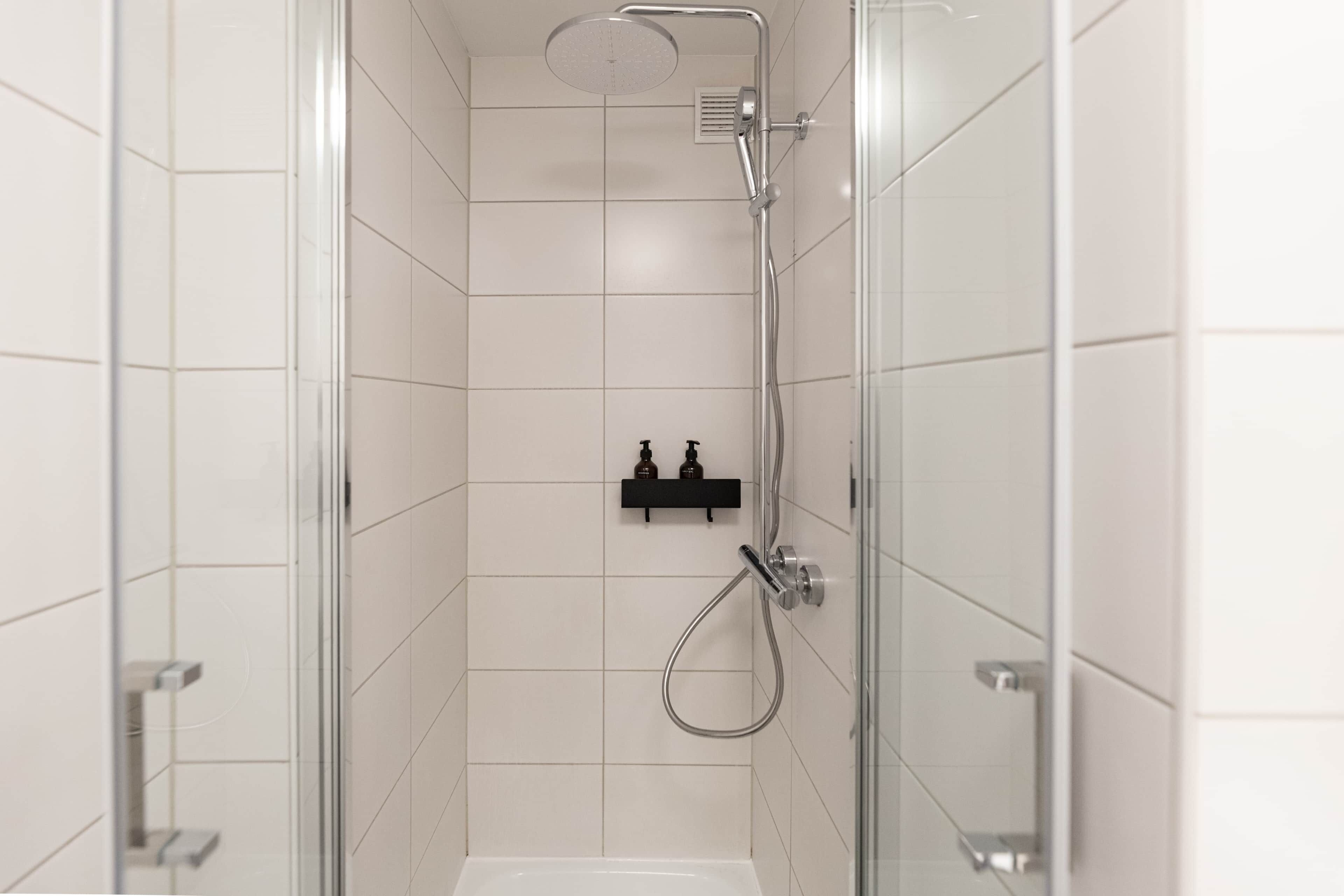 Een moderne douche met een glazen deur, een handdouche en een muurbevestigde kraan.