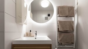 A modern bathroom with a white vanity, a round mirror with integrated lighting, and a towel rack with folded towels.