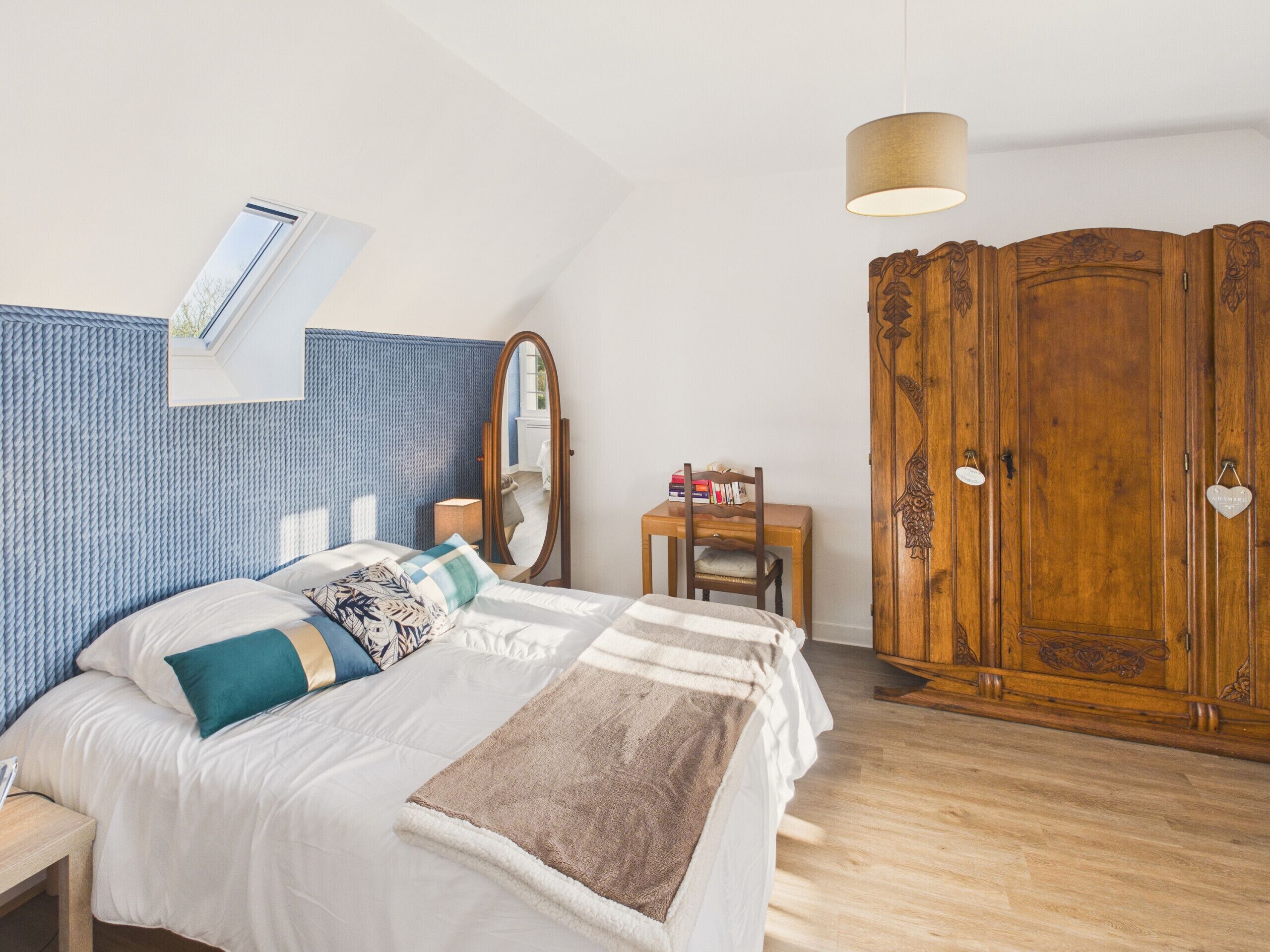 Ein Schlafzimmer mit einem Bett, einem Holzschrank, einem Schreibtisch und einer Pendelleuchte.