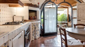 Een keuken met een betegelde spatwand, een fornuis en een eethoek met een tafel en stoelen.