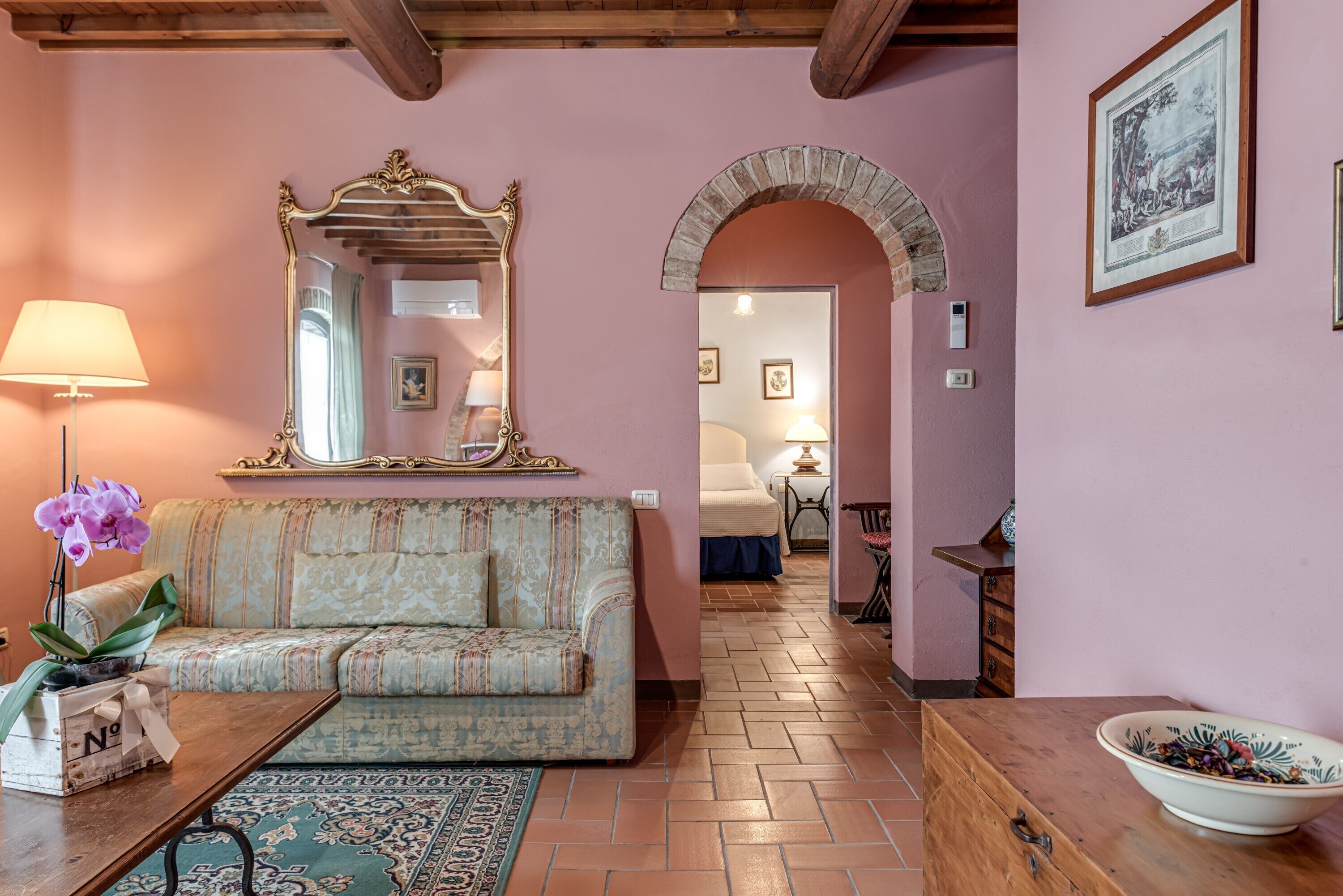 Una stanza con un divano, uno specchio, una lampada, una ciotola e un tappeto decorato.