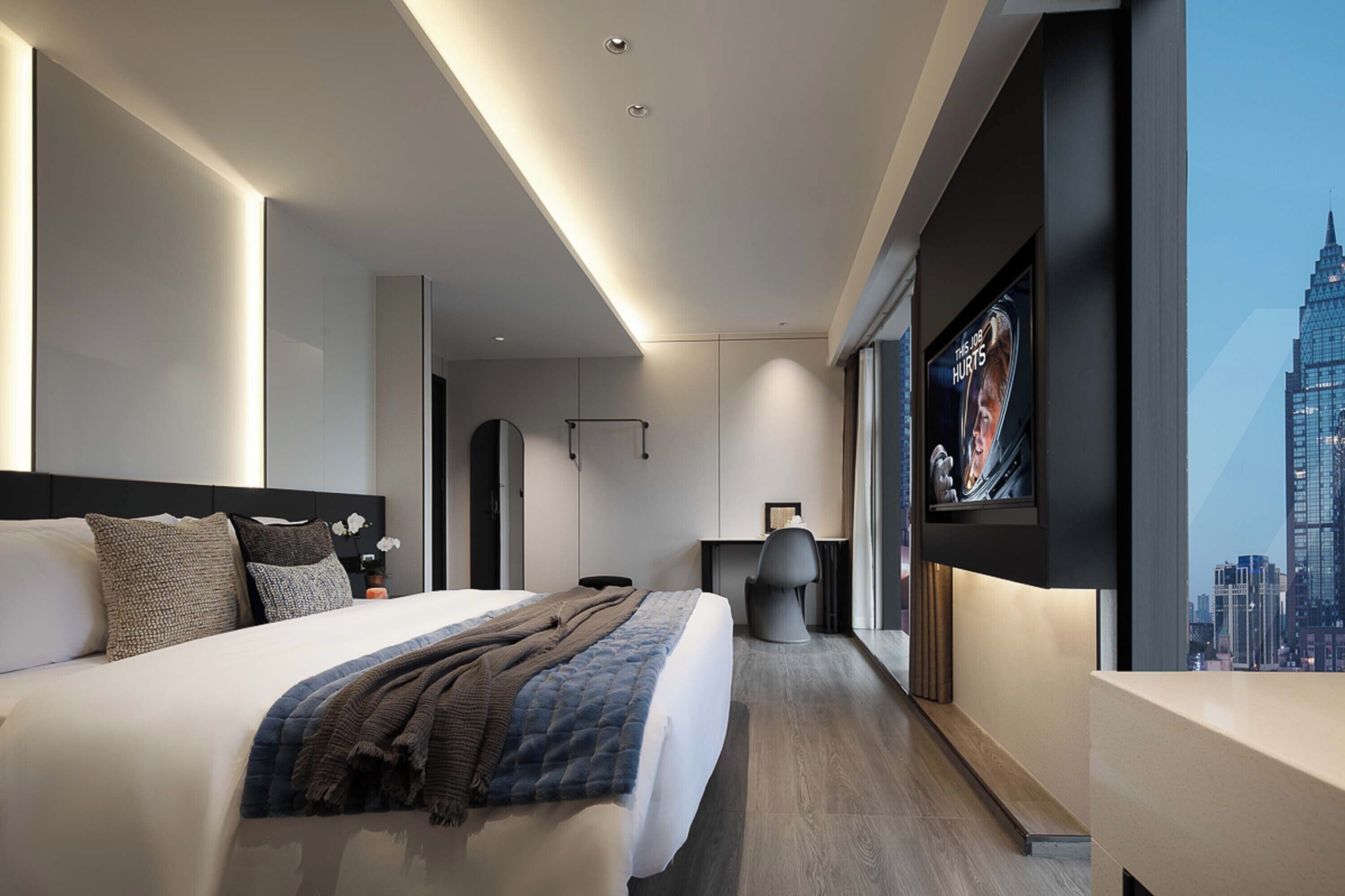 A modern hotel room with a large bed, a desk, and a city view.