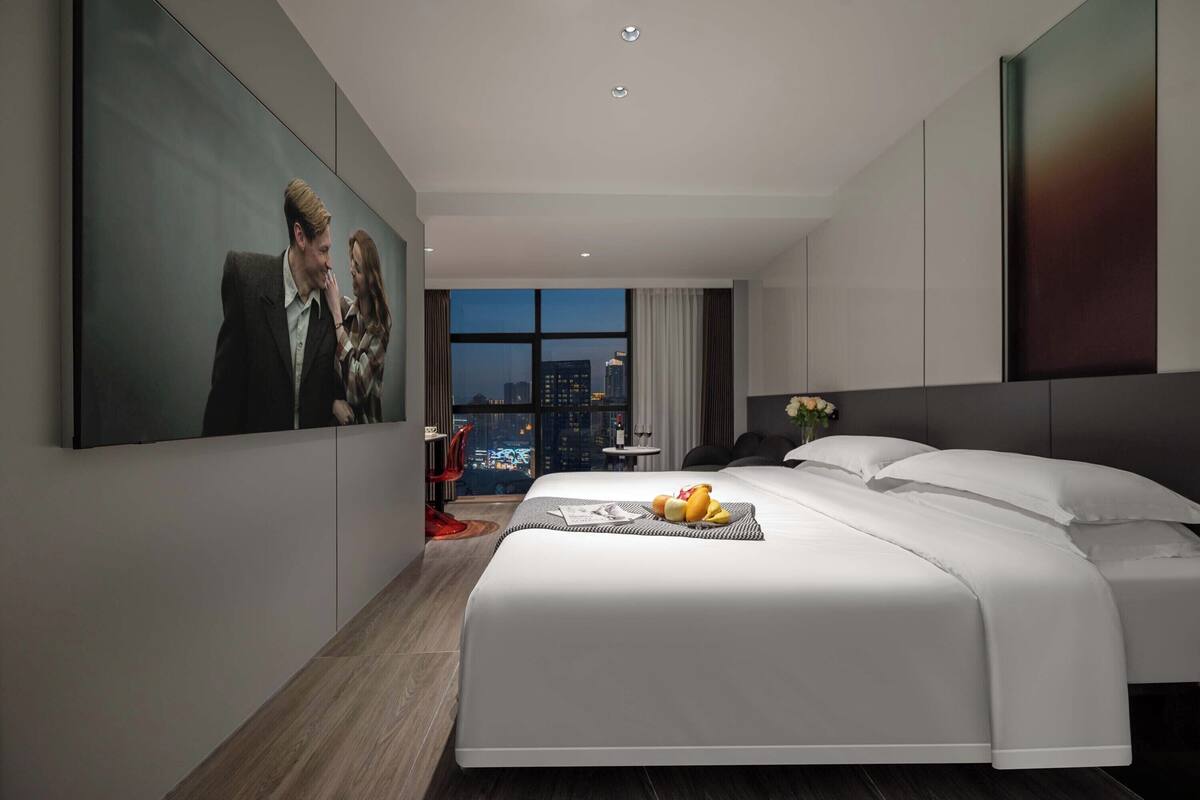 Quarto de hotel moderno com uma cama grande, vista para a cidade e um quadro na parede.