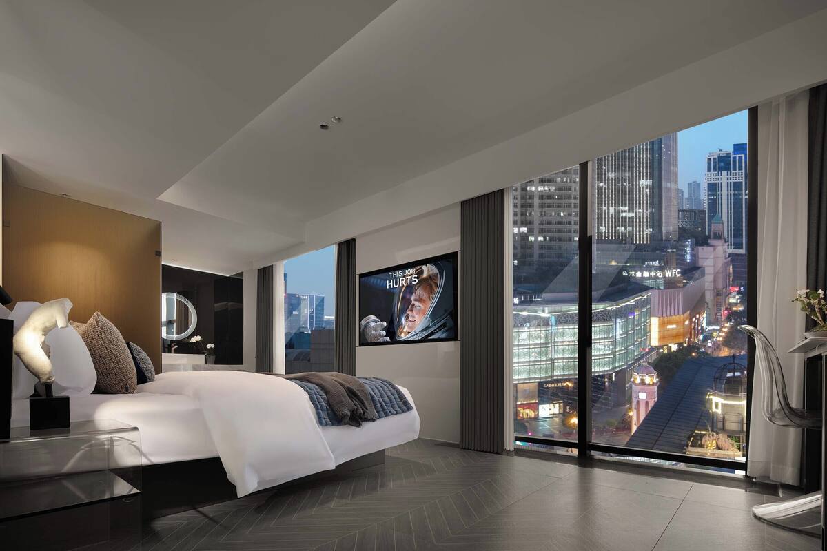 Quarto de hotel moderno com uma cama grande, televisão e vista para a cidade.